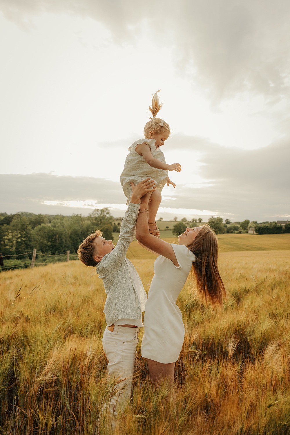 Papa et maman lançant leur petite fille vers le ciel dans un champ de blé doré, photographe famille Mayenne